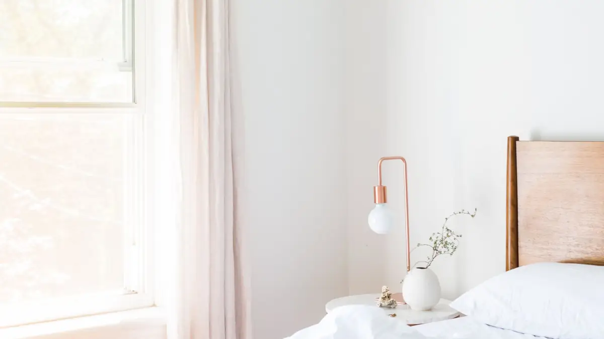 Bright white bedroom with a bedside lamp and soft morning light