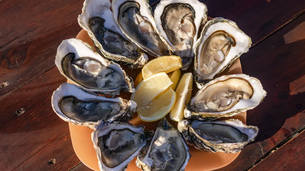 A dozen fresh oysters on the half shell with lemon wedges, the food highest in zinc