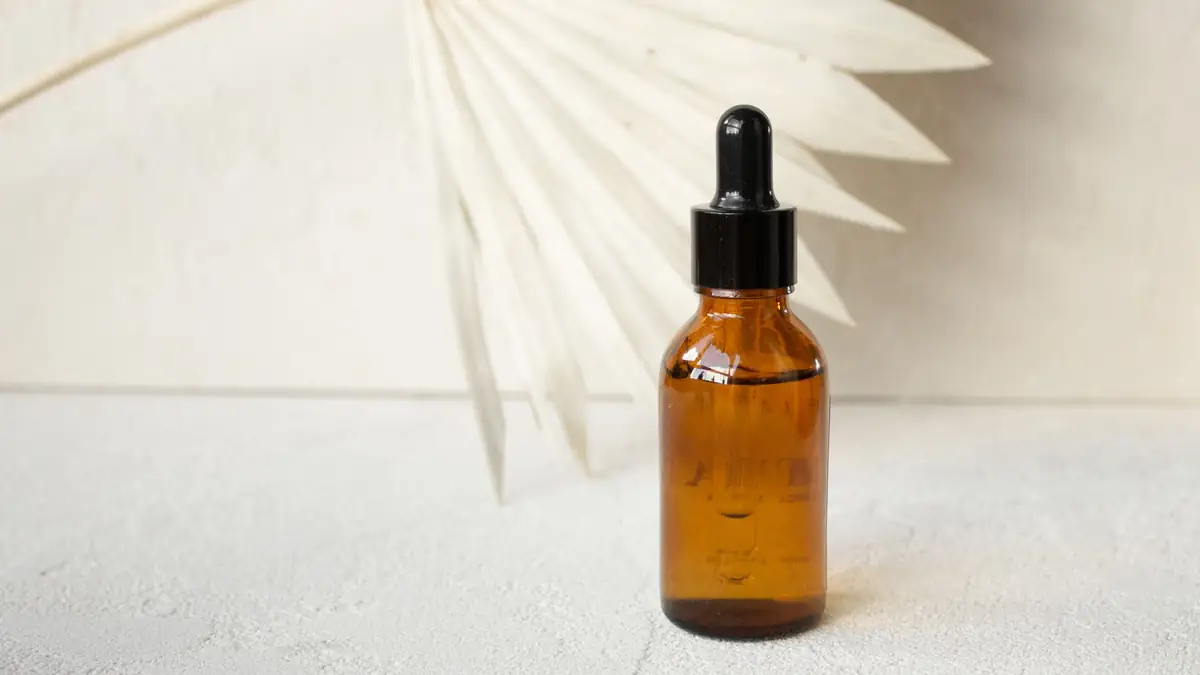 An unlabeled amber glass dropper bottle in front of a dried palm leaf