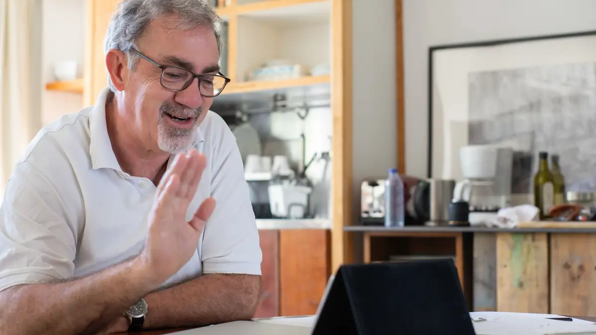 Smiling older man waving at a laptop on a video call